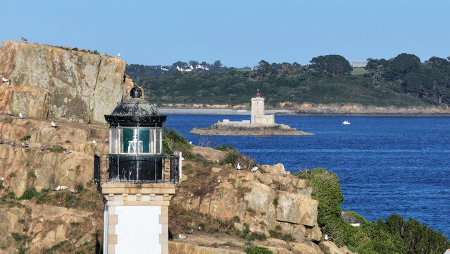 Aerial view of two lighthouses standing sentinel on rugged, sun-drenched cliffs overlooking the deep blue sea, Carantec, Brittany, France.