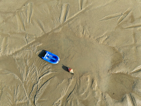 Aerial view of a lone blue toy boat and a small orange object stranded on the rippled, sandy shores of the coast, Bourcefranc-le-Chapus, France.