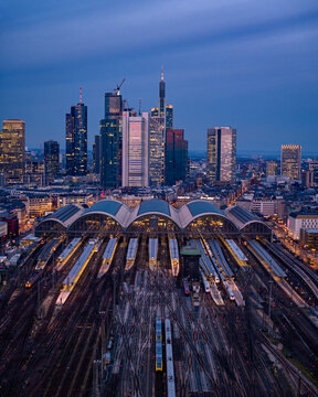 Aerial view of Frankfurt Hauptbahnhof railway station with its arched glass roof, nestled amidst the city's towering skyscrapers piercing the twilight sky, Frankfurt am Main, Hessen, Germany.