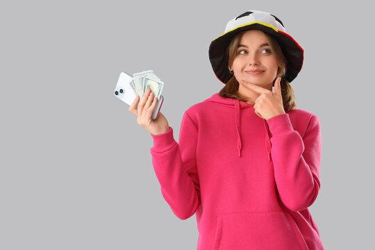 Thoughtful young woman with money and mobile phone on light background. Sports bet concept