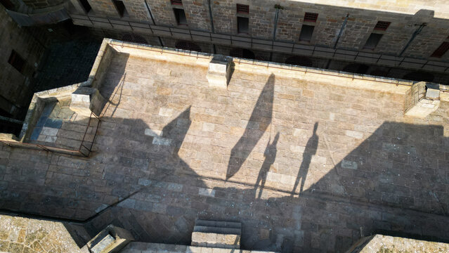 Aerial view of the ancient stone courtyard of Chateau du Taureau, bathed in golden light, casting long, stark shadows against the rugged texture, Plouezoc'h, Bretagne, France.