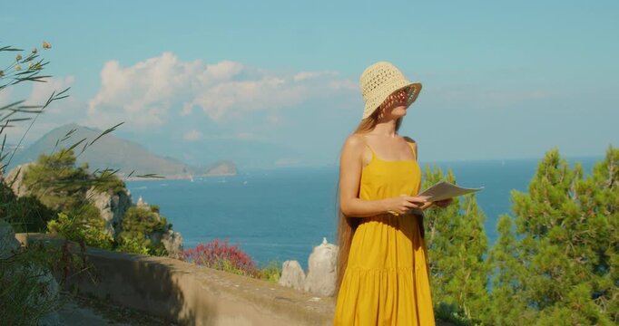 Woman with a map enjoys a sunny summer sea view from a scenic lookout