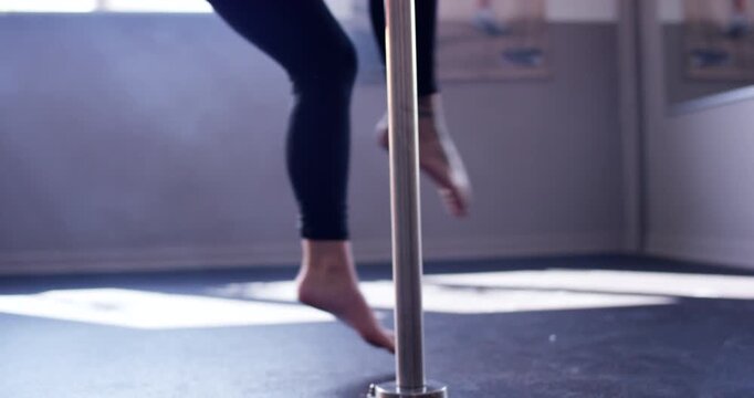 Close up of person feet performing dance moves on floor next to vertical metal pole in gym