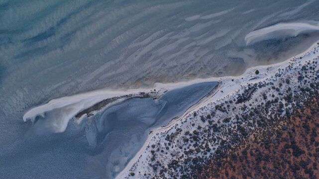 Aerial view of where the turquoise waters meet the rugged, earthy coastline, creating a mesmerizing contrast of colors and textures, Denham, Western Australia, Australia.