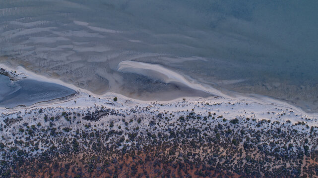 Aerial view of the dramatic transition from the deep reddish earth, through a narrow strip of white sand, to the shallow, pale blue-green waters, Denham, Western Australia, Australia.