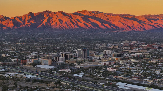 Aerial view of Tucson's cityscape, backed by the Santa Catalina Mountains ablaze in sunset orange, Tucson, Arizona, United States.