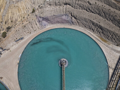 Aerial view of vibrant turquoise waters in a massive circular industrial pond, contrasting sharply with the scarred, arid earth of the surrounding landscape, Tucson, Arizona, United States.