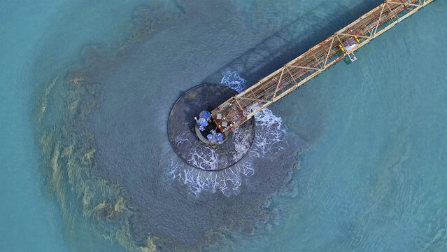 Aerial view of a rusty industrial structure discharging a murky plume into vibrant turquoise waters, Tucson, Arizona, United States.
