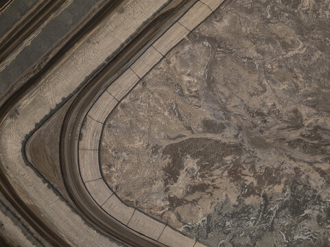 Aerial view of a stark, curving industrial path cutting through a vast expanse of disturbed earth, revealing varied textures and muted tones, Tucson, Arizona, United States.