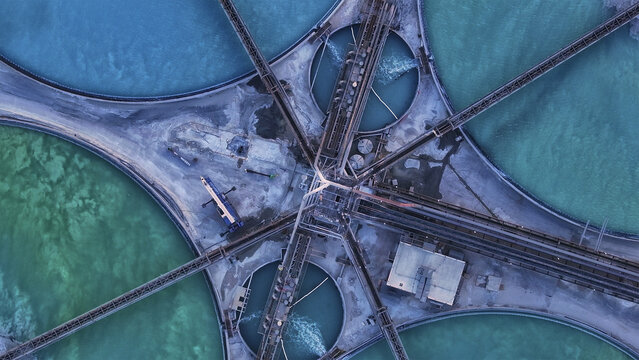 Aerial view of vibrant turquoise and emerald industrial pools, crisscrossed by stark grey conveyors, creating a striking geometric pattern, Tucson, Arizona, United States.