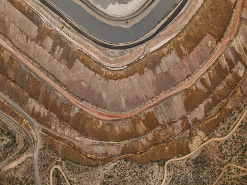 Aerial view of a vast terraced open-pit mine, revealing dramatic layers of ochre and rust-colored earth descending to a dark pool, Tucson, Arizona, United States.