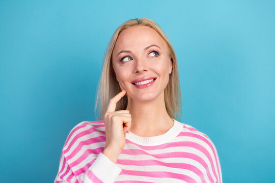Thoughtful smiling woman in pink striped sweater looking up on blue background, casual portrait of a blonde thinking and optimistic expression