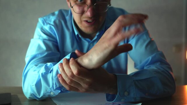 Businessman in a blue dress shirt massages his wrist, reacting to pain after prolonged typing and mouse use. Concept of repetitive strain and office-related injury.