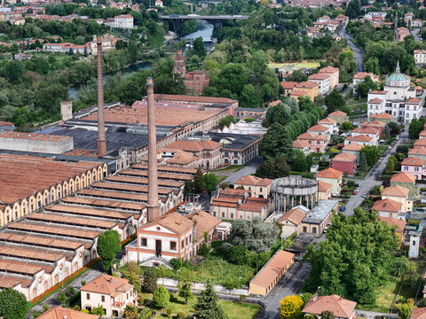Aerial view of the Industrial Village of Crespi d'Adda with its iconic tall brick chimneys, terracotta rooftops, and lush green trees in Capriate San Gervasio, Lombardia, Italy.