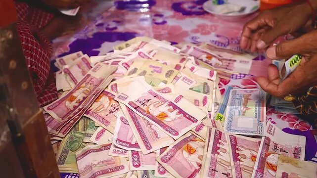 Close-up view of people counting a massive heap of Myanmar Kyat (MMK) banknotes on a table. The pile consists mainly of 5,000 and 10,000 Kyat bills. 