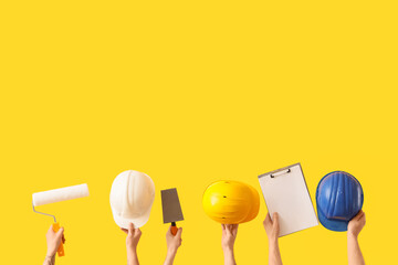 Male hands with painter's tools, hardhats and clipboard on yellow background © Pixel-Shot