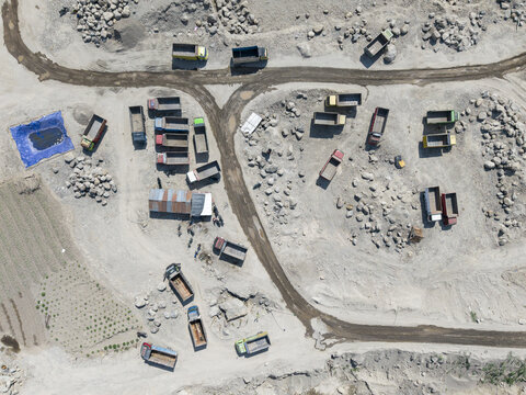 Aerial view of a bustling open-pit quarry, where numerous trucks move along dusty tracks amidst vast piles of crushed stone, Klaten, Central Java, Indonesia.
