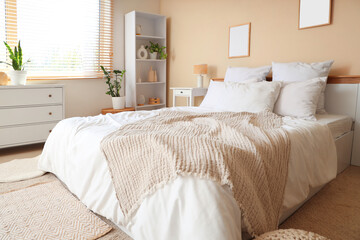 Fototapeta premium Interior of light bedroom with cozy bed, houseplants and bedside table