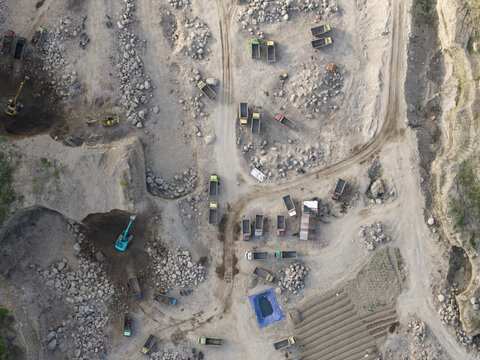Aerial view of a sprawling open-pit quarry with heavy machinery carving into the raw earth, revealing deep contrasts of light and shadow, Klaten, Central Java, Indonesia.