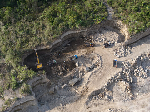 Aerial view of heavy machinery carving into the earth, revealing raw textures and tones amidst vibrant green foliage, Klaten, Central Java, Indonesia.