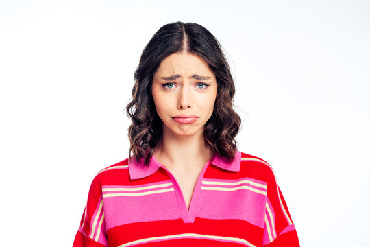 Sad young woman in pink and red striped sweater making a pouty face in a close-up portrait expressing disappointment and vulnerability on a white background
