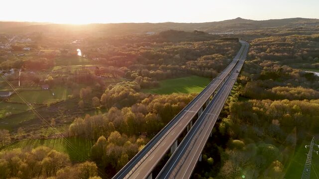 Aerial view of Viaducto Arnoia bridge spanning over a dense forest and green fields during golden hour in Allariz, Province of Ourense, Spain.