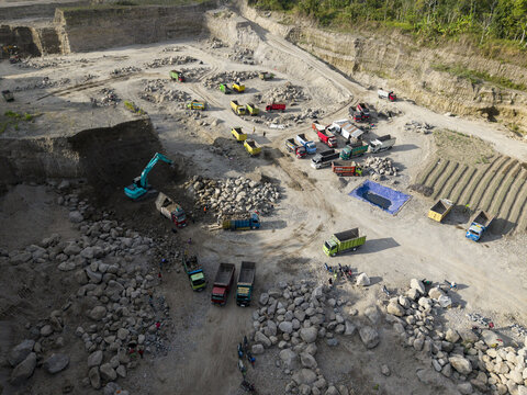 Aerial view of a large, active open-pit quarry, where excavators and dump trucks move vast amounts of dry, rocky material, Klaten, Central Java, Indonesia.