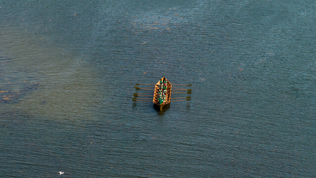 Aerial view of a solitary green and brown fishing trap structure floating on the deep, tranquil blue-green waters, Hiittinen, Southwest Finland, Finland.