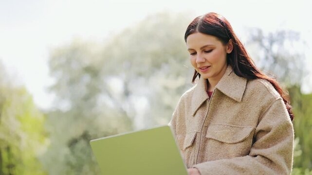 Happy woman finds joy and focus working on laptop outdoors. Contentment fills face, enjoying nature's tranquility while being productive. Represents remote work, freedom, and pleasant lifestyle.
