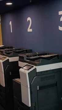 Vertical shot of multifunction printers and copiers arranged in row inside modern office, ready for document processing