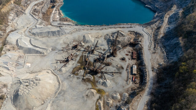Aerial view of a vast quarry, where grey rock and heavy machinery starkly contrast with the vibrant turquoise water of an adjacent pit, Tomkins Cove, New York, United States.