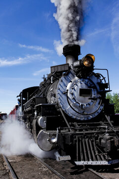 Steam locomotive front view with smoke against blue sky