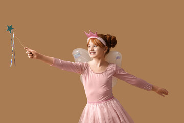 Naklejka premium Cute girl in fairy costume playing with magic wand on brown background