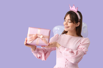 Naklejka premium Young woman in fairy costume with gift box on lilac background