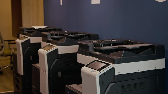 Row of modern multifunction laser printers lined up against blue wall in corporate office or coworking space