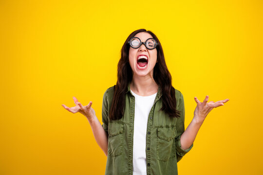 Young woman screaming in frustration wearing round glasses against a bright yellow background