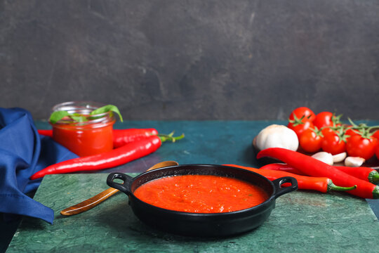 Frying pan of tomato sauce with chili peppers and garlic on dark table