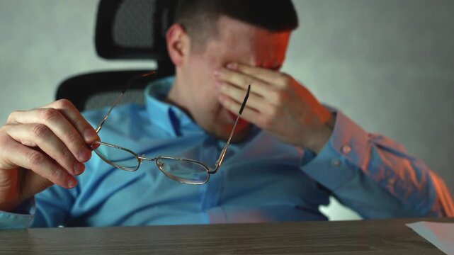 Young professional suffering from tired eyes, taking break while working late. Eye strain and stress from prolonged computer use in office