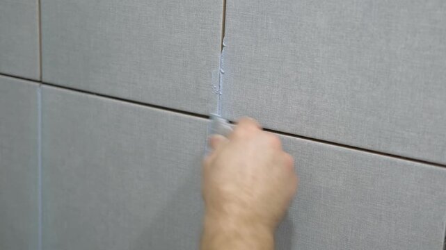 Worker using a rubber grout float to smooth grout between tiles. Carefully applying sealant to tiles joints. Workman hands smoothing caulk, using small tool to remove excess and create clean seam.