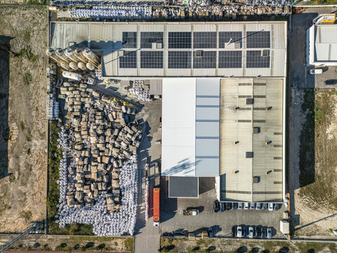 Aerial view of a large industrial building with solar panels on the roof, surrounded by stacks of materials and parked vehicles, Vagos, Aveiro, Portugal.
