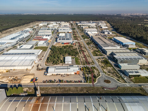 Aerial view of the sprawling Zona Industrial de Vagos, where modern, gleaming rooftops contrast with verdant borders under a crisp blue sky, Vagos, Aveiro, Portugal.