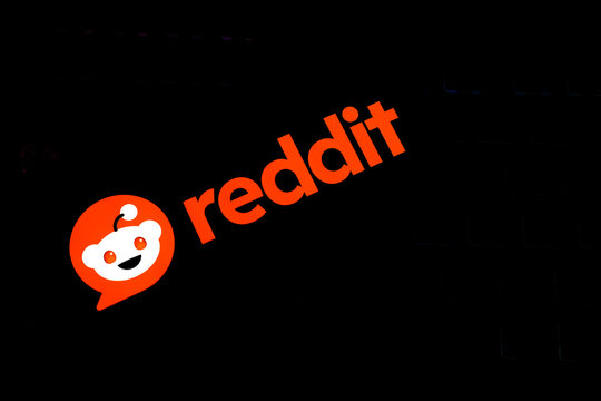  Reddit Logo and Wordmark in Vibrant Orange and White, Glowing Against a Dark Textured Keyboard Background, Illustrating Online Communities, Social Media Discussion, and Digital Content Sharing.