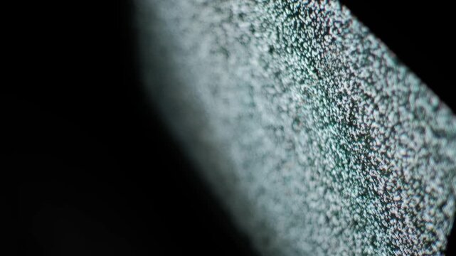 A macro close-up captures flickering grain of analog TV static noise on a dark screen. Concept of technical difficulties, signal loss, retro technology, and abstract digital interference.