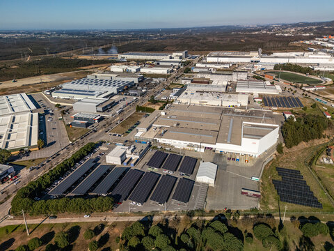 Aerial view of a sprawling industrial park with dark solar arrays contrasting against the light grey rooftops and lush green perimeter, Albergaria-a-Velha, Aveiro District, Portugal.