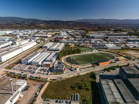 Aerial view of industrial zone with grey buildings, contrasting sharply with a green sports field and orange track, Albergaria-a-Velha, Aveiro District, Portugal.
