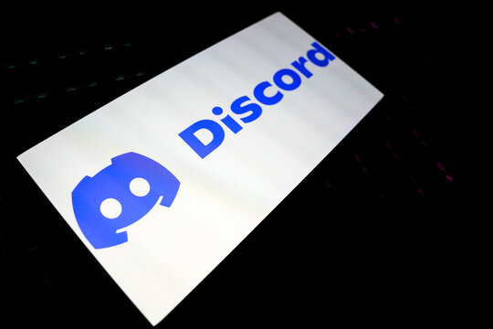 Discord Logo and Wordmark on a Bright White Smartphone Screen Tilted Over a Dark Keyboard, Representing Social Communication, Online Communities, Instant Messaging, and Digital Gaming Culture.