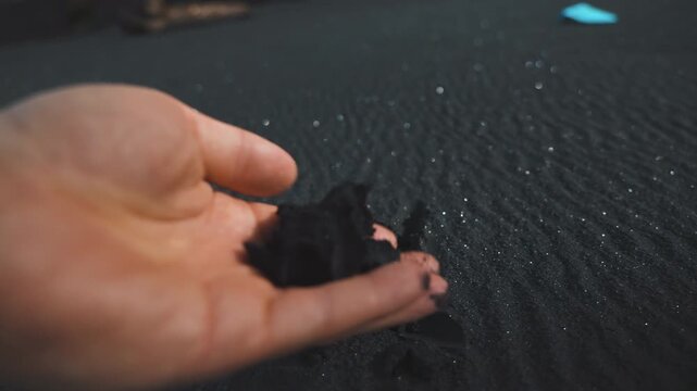 Close Up of Hand Scooping Black Volcanic Sand on Beach