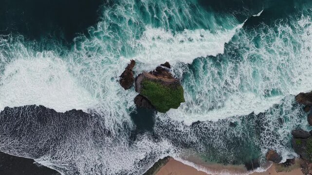 Aerial view of Mesra Beach featuring powerful ocean waves crashing against a green rocky island and sandy shore Kecamatan Tanjungsari, Daerah Istimewa Yogya, Indonesia.