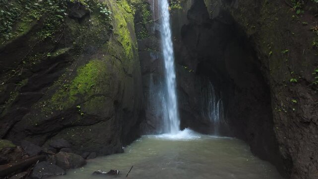 Camera Tilting Down Over Tropical Waterfall in Rocky Jungle Canyon
