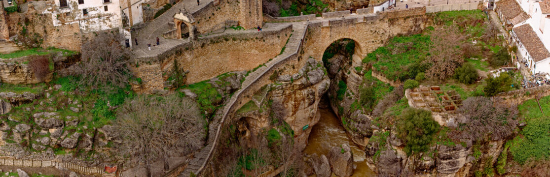 Aerial view of the Puente Nuevo bridge spanning a deep gorge, its stone contrasting with the lush green vegetation, Ronda, Andalusia, Spain.